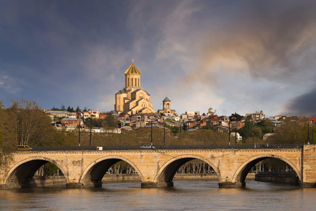 Ancient arched bridge and Sameba Cathedral in Tbilisi, Georgia